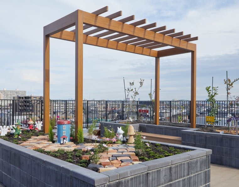 木製パーゴラと植栽のある屋上庭園。都市景観が見える共用スペース