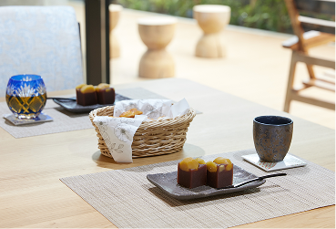明るい食堂で整えられたテーブル。籐籠のパン、焼菓子、飲料が配置されている。