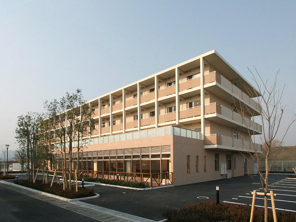介護施設の外観。ベージュ系タイル張りの4階建て建物、駐車場完備。